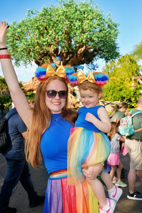 George's wife holding their daughter, both in matching rainbow outfits at Disney