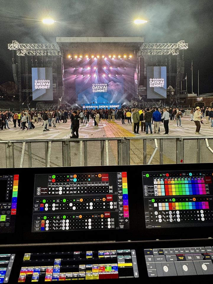 Stadium stage with summit screens seen over a grandMA3 console at front of house